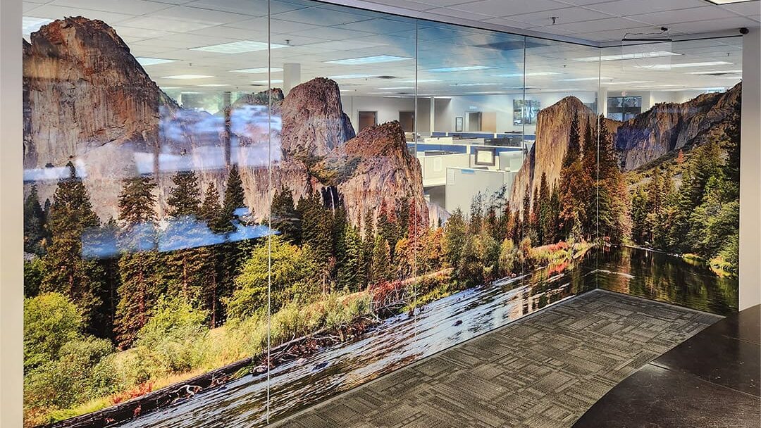 Window decals depicting a mountain and stream landscape cover an internal glass wall inside an office building.
