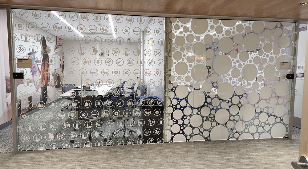 Two offices side by side with front-facing glass walls covered in artfully designed window decals for privacy.