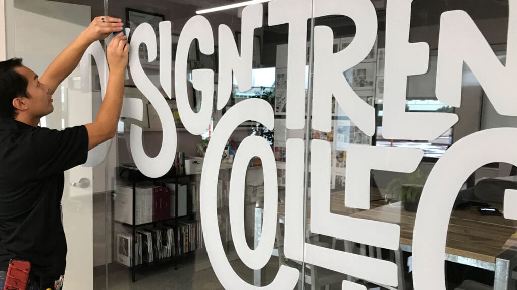 A Brand Ink installer places vinyl decals on an internal window in an office space.