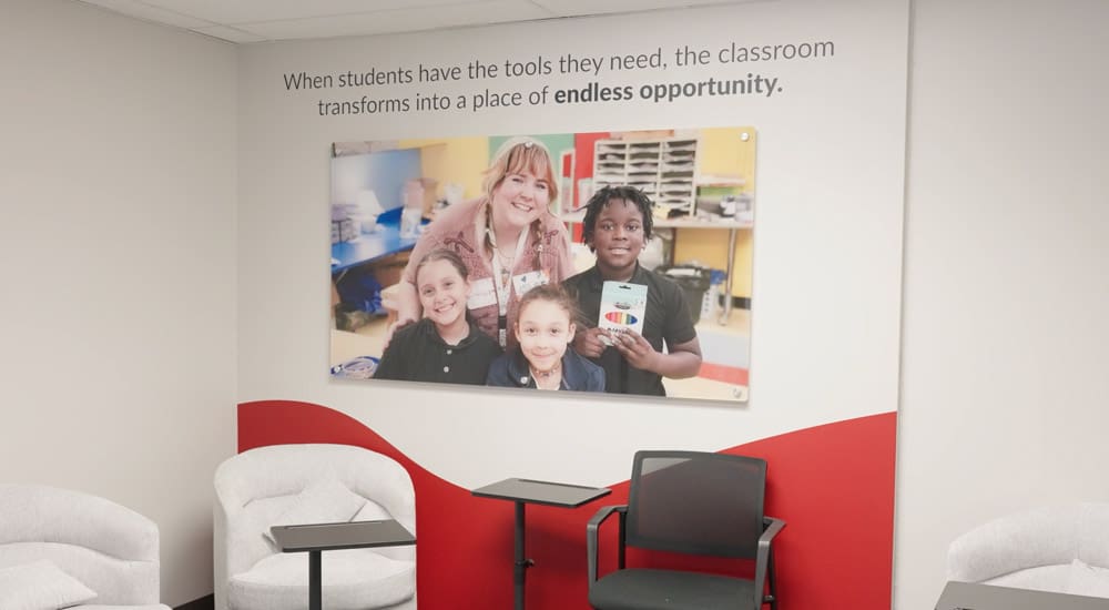 Brand ink installed a vinyl decal over a wall in Kids In Need Foundation's headquarters: It is a picture of a teacher standing with several students. Over the image reads "When students have the tools they need, the classroom transforms into a place of endless opportunity."