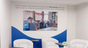 Brand ink installed a mounted printed acrylic on a wall in Kids In Need Foundation's headquarters: It is a picture of three students sitting at a table in a classroom. Over the image is a vinyl decal that reads "School supplies help students unlock their full potential. With the right resources, students are equipped to learn, grow, and dream big."