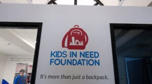 The Kids in Need Foundation logo above a statement that says "It's more than just a backpack" is installed on a white wall between two doorways.